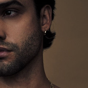 Man with tattoos wearing multiple necklaces and a Calvin Klein underwear on a brown background