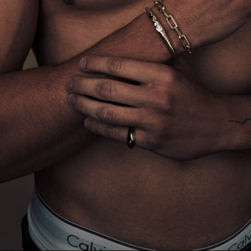 Man with tattoos wearing multiple necklaces and a Calvin Klein underwear on a brown background