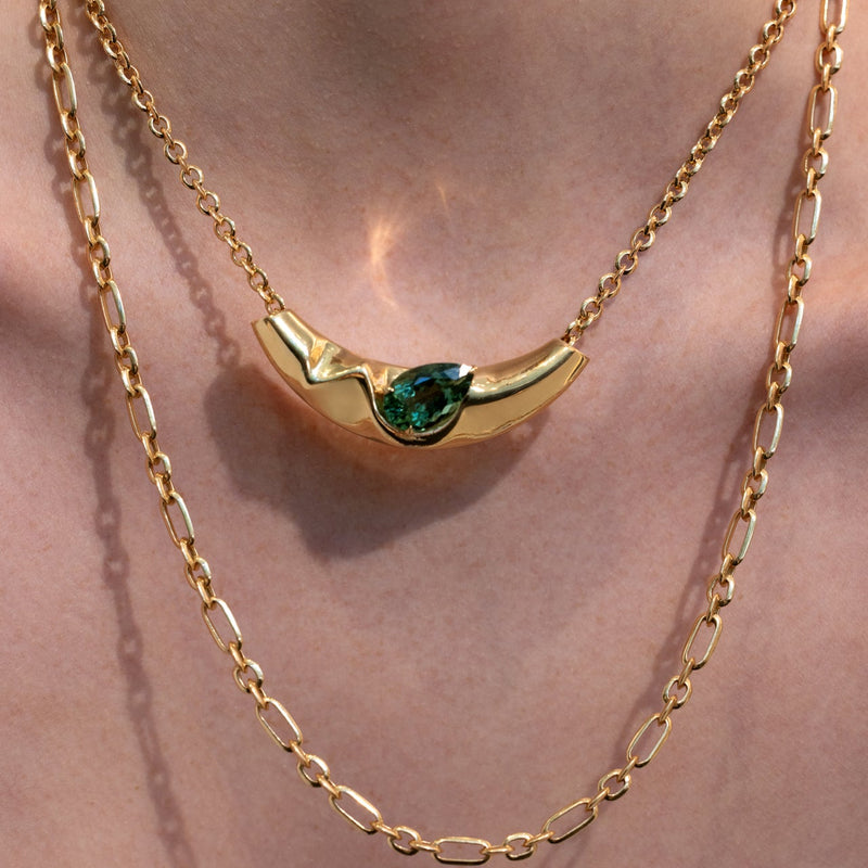 Gold necklace with a green gemstone on a white background