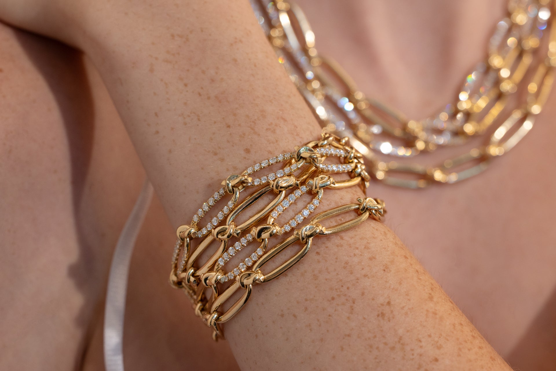Close-up of a person's arm wearing multiple gold bracelets with a blurred background